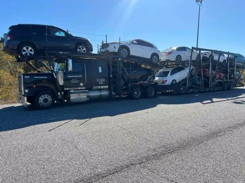Black commercial car transport carrier truck hauling sedans and SUVs on a highway route toward Vancouver from Calgary.