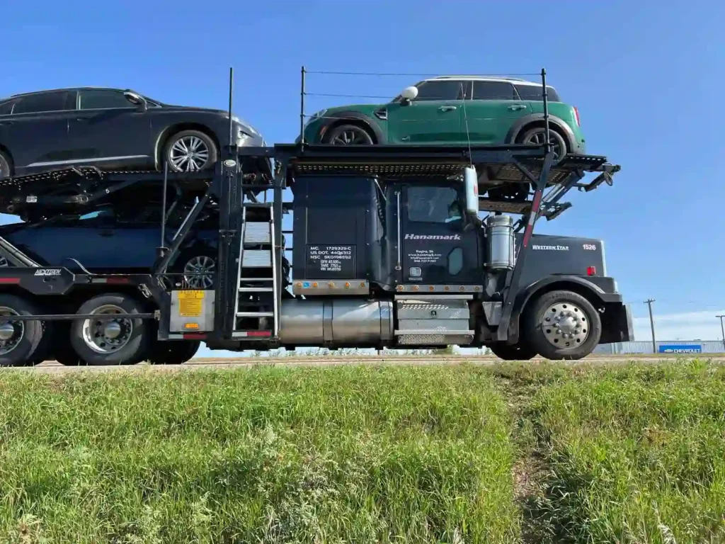 Black Western Star auto transport truck hauling a green Mini Cooper on a long-distance route from Saskatoon to Toronto.